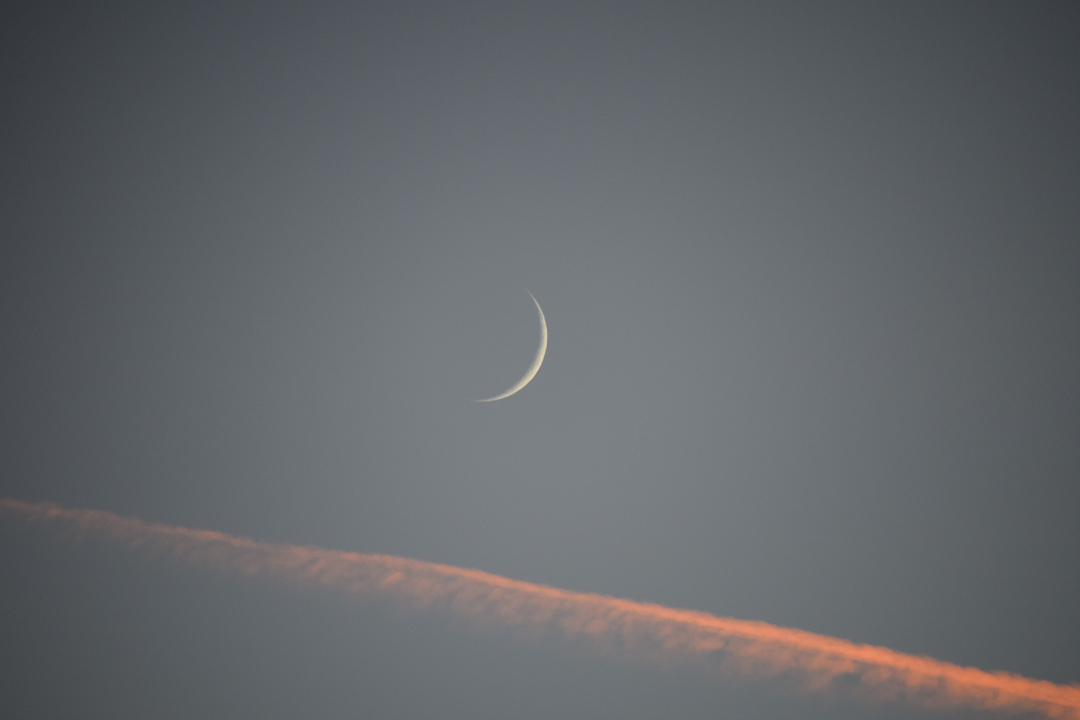 Crescent moon with contrail at sunset
